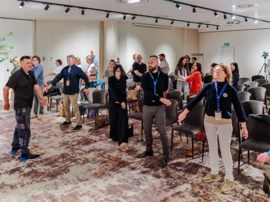Deelnemers voeren HypnoQiGong-bewegingen uit tijdens een live demonstratie op het Hypnotic-congres in Gent, 2025.