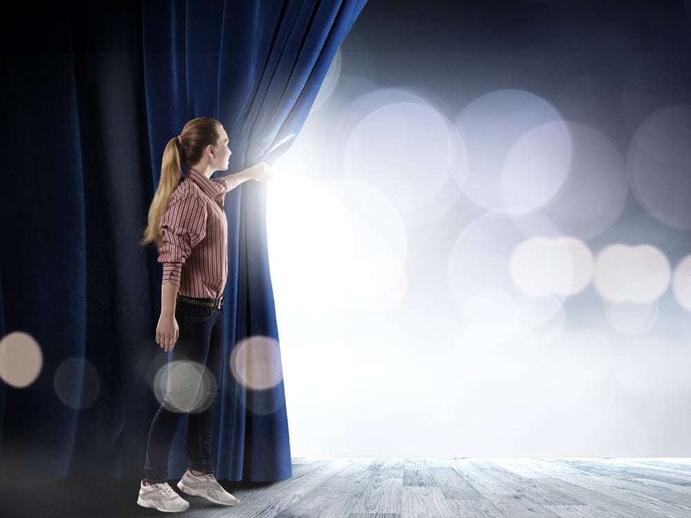 Een vrouw opent het gordijn naar een verlicht podium.