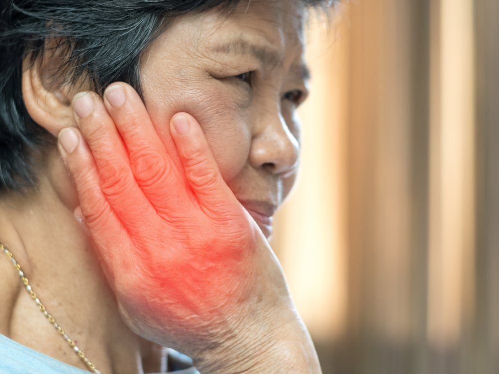 Tandenknarsen stoppen met Hypnotherapie 2 Een persoon houdt een hand tegen de kaak, met rood gemarkeerde pijnzone.
