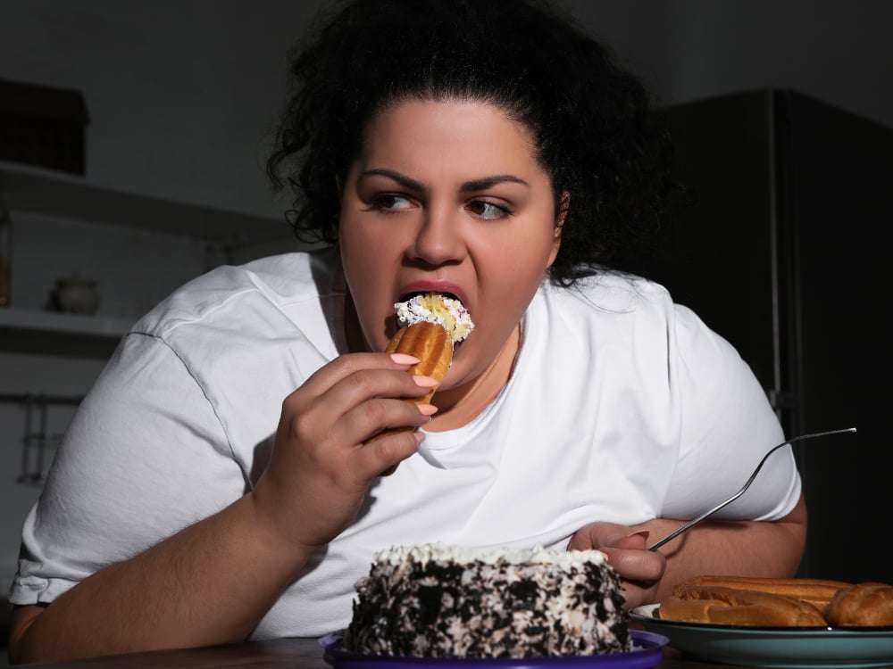 Binge-eten behandelen met Hypnose 2 Een vrouw eet gebak aan een tafel.